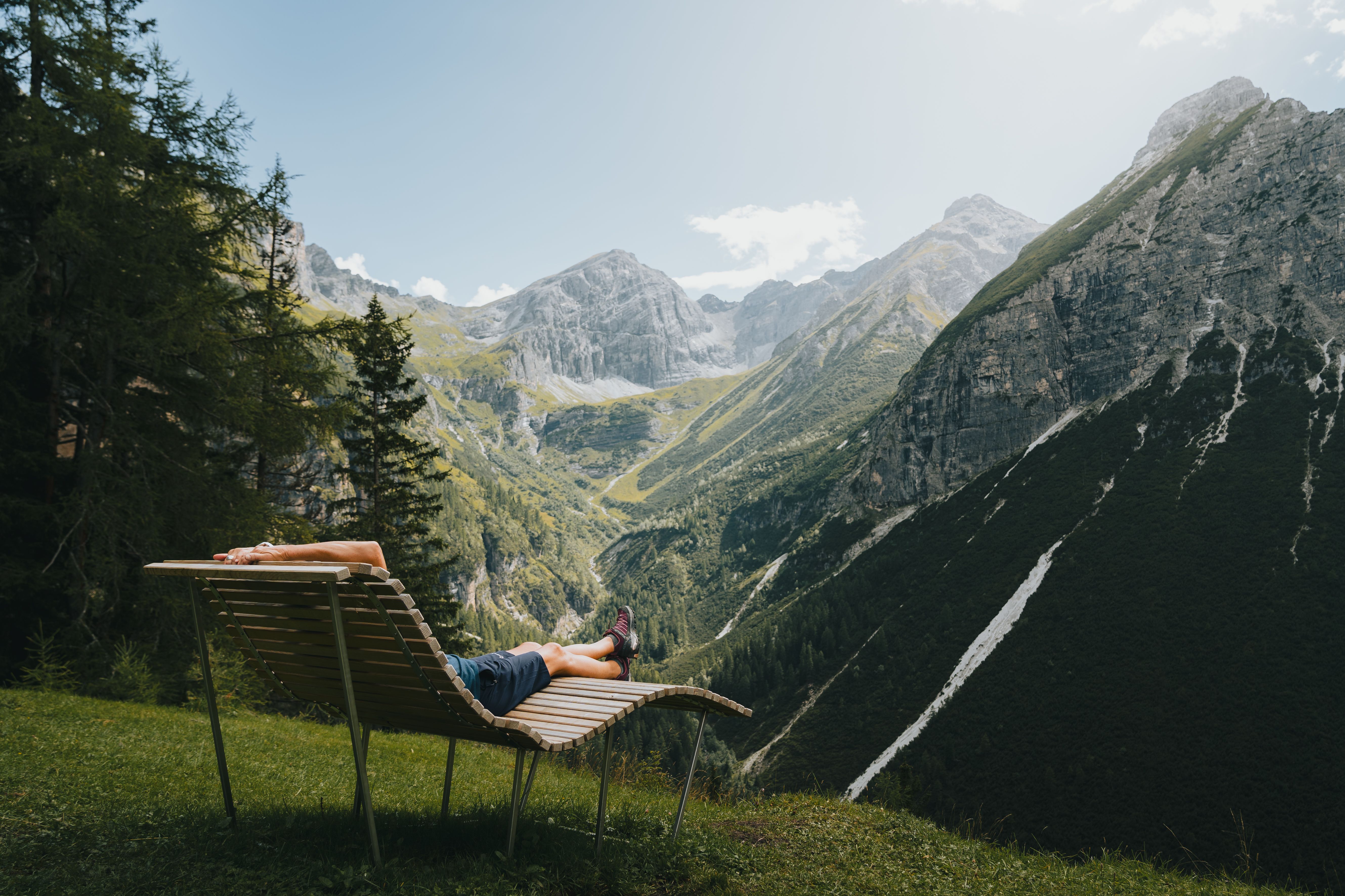 Wanderer ruht sich auf Bank aus und schaut in das Bergpanorama