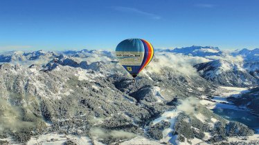 The blue skies are dotted with the bright colours of the balloons as they float above the scenic Alpine valley’s winter wonderland below, © Tourismusverband Tannheimer Tal